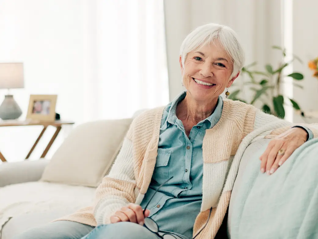 Seniorin sitzt daheim auf ihrem Sofa.