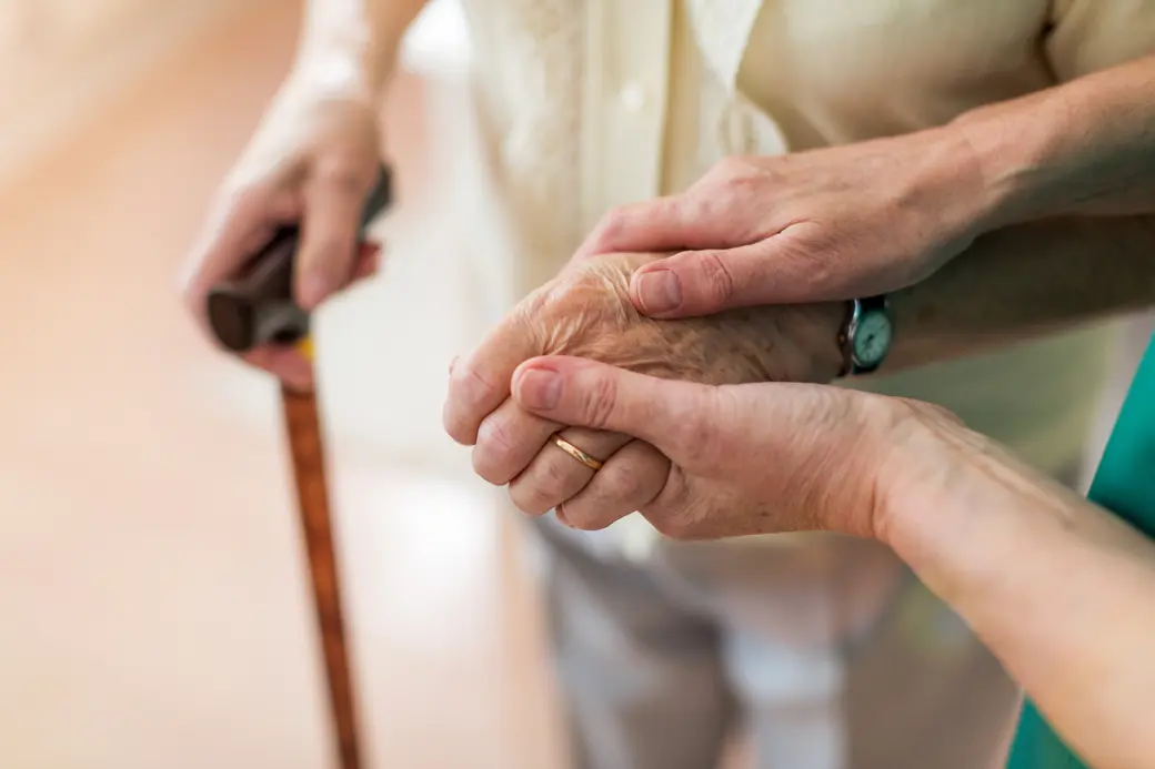 Krankenschwester hält die Hände einer älteren Patientin.